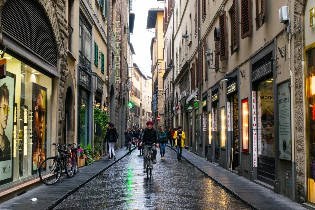 man riding a bike toward the camera on a rainy day on a side street in florence italy