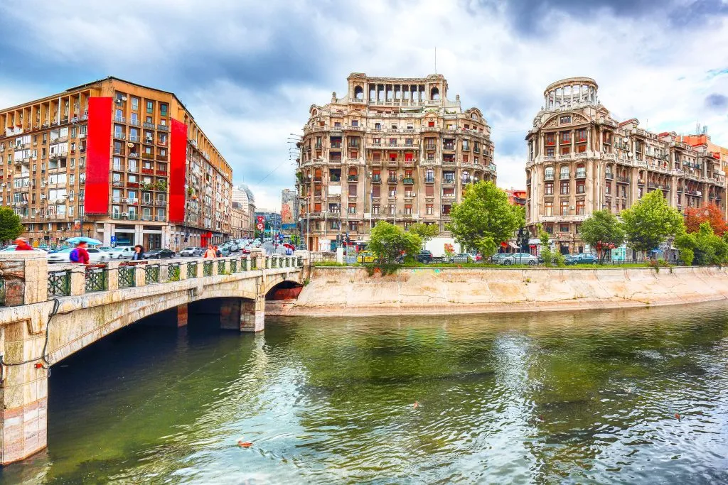 view of historic buildings in bucharest romania from across the river with a bridge in the left foreground