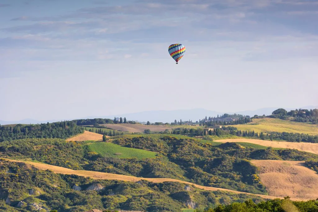 hot air balloon in the distance over the tuscany countyside, a bucket list tuscany travel experience