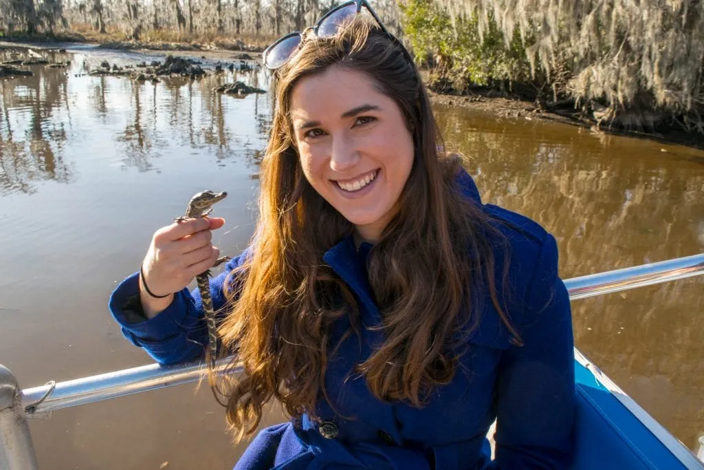 Kate Storm in a blue coat holding up a baby alligator on a bayou tour during a 3 day New Orleans itinerary