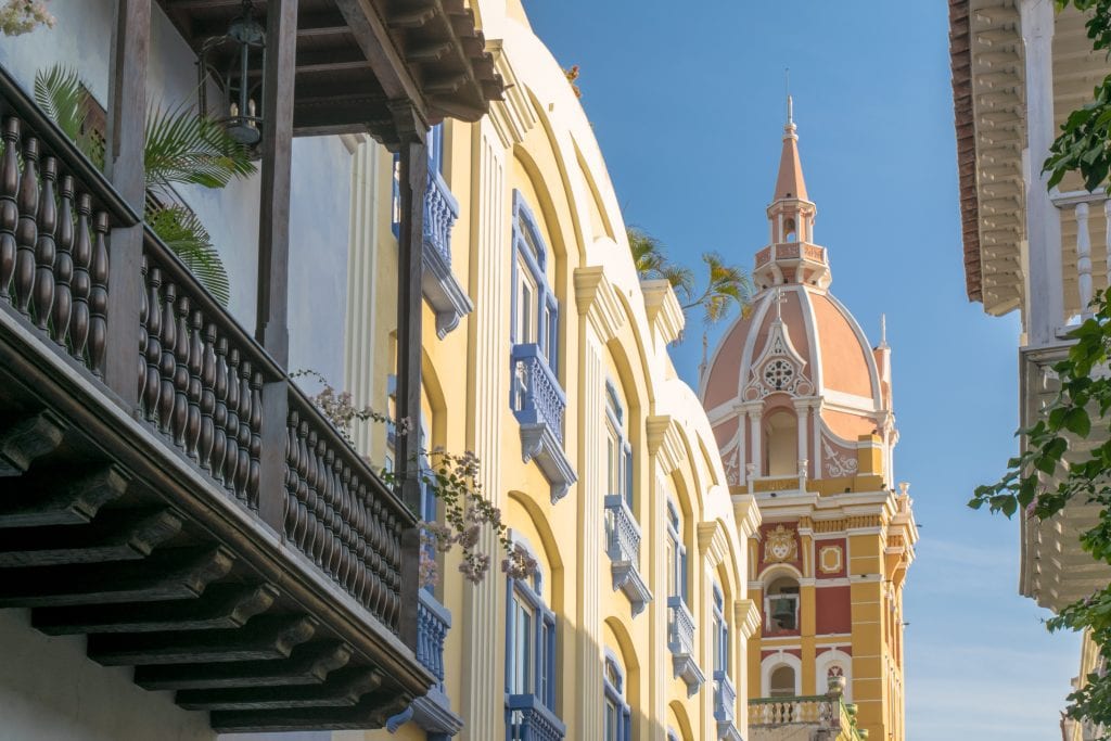 Colorful buildings of Cartagena Colombia with a church steeple in the distance.