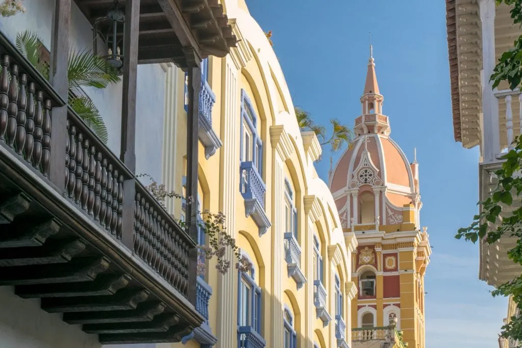 Colorful buildings of Cartagena Colombia with a church steeple in the distance.