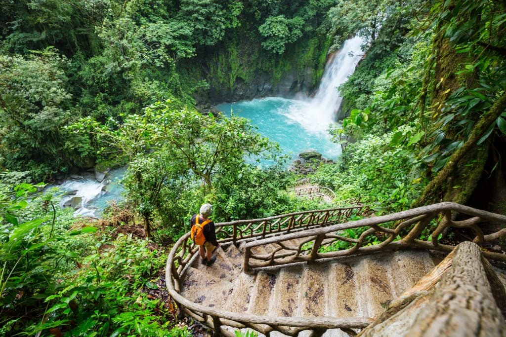 woman walking down a staircase to a waterfall in costa rica