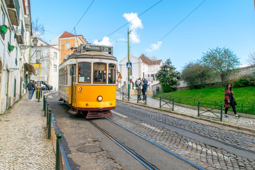 Bright yellow tram ascending a hill in Lisbon Portugal on a sunny day--be sure to take plenty of pretty tram photos during your one day in Lisbon!