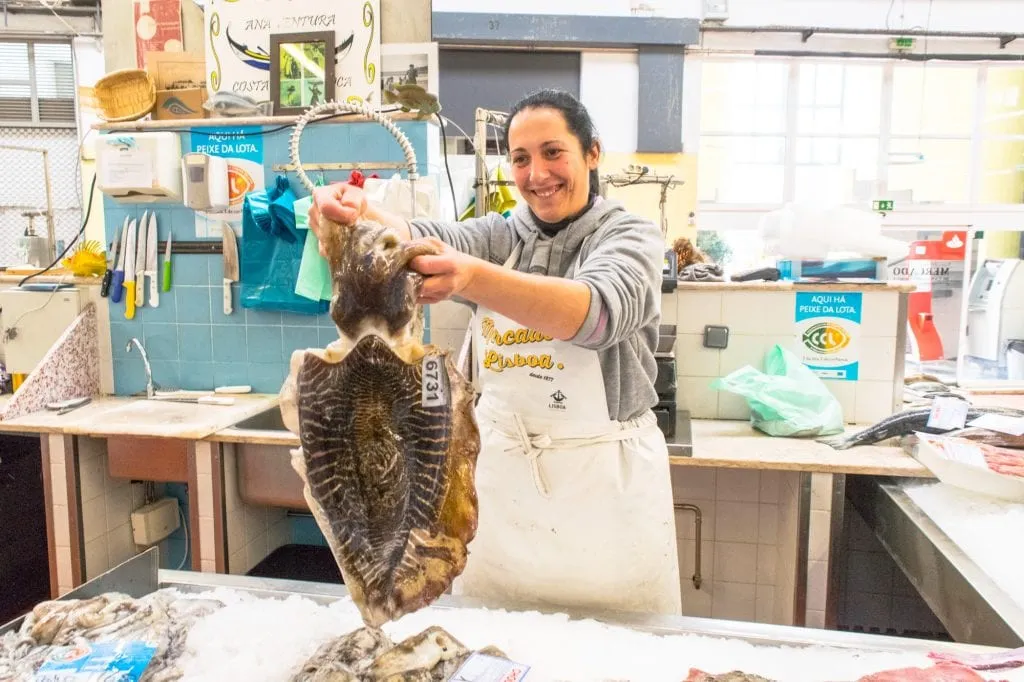 woman holding up a large, raw fish in the campo de ourique market