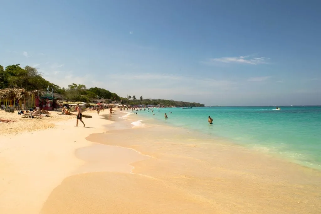 Playa Blanca in Colombia as seen looking down the beach with the turquoise sea on the right and golden sand on the left
