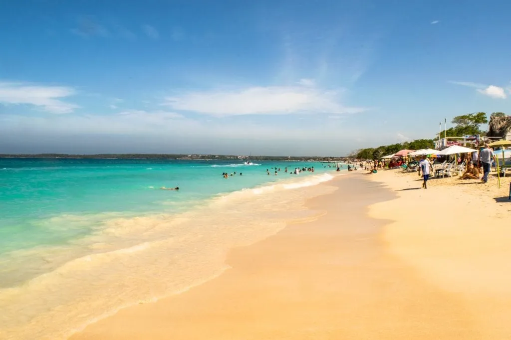 Playa Blanca, Isla Baru, Cartagena, Colombia. The water is on the left and a group of umbrellas with people resting under them to the right.