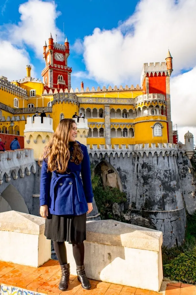 kate storm in a blue coat standing in front of pena palace during a day trip to sintra from lisbon in march