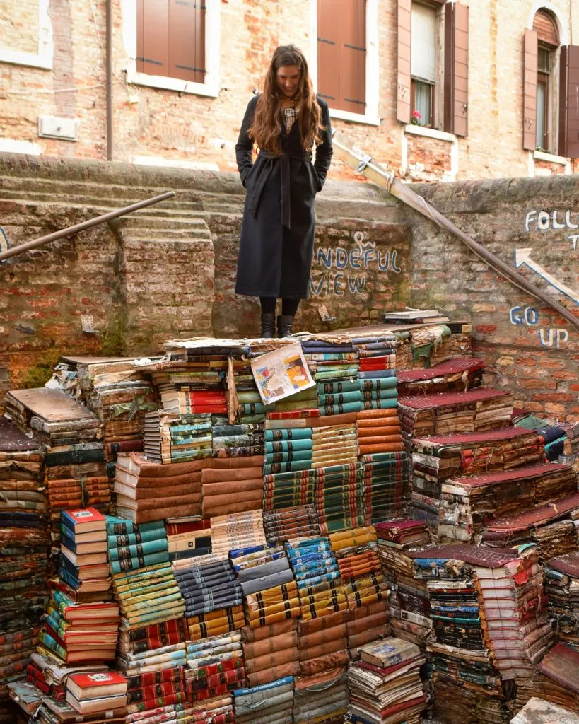 kate storm standing on top of a staircase of books at libreria acqua alta venice italy