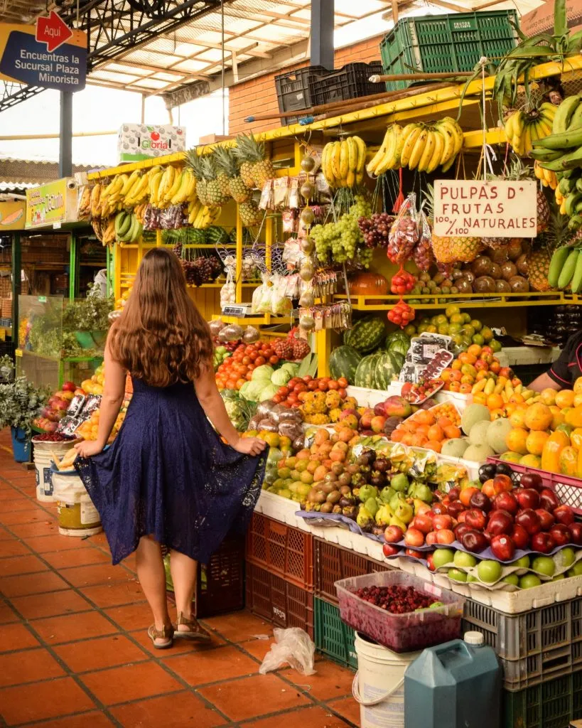 kate storm in a blue dress in front of a fruit stand in medellin colombia