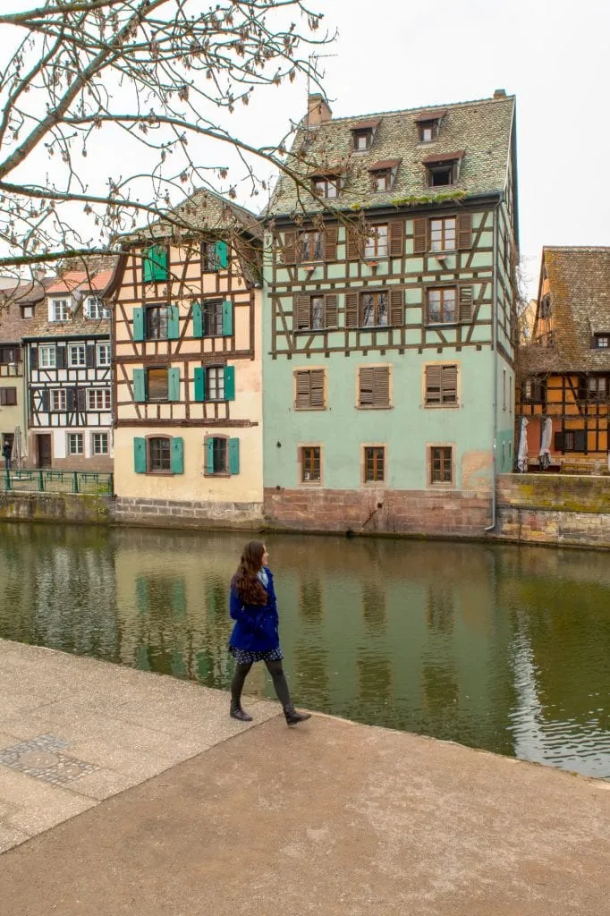 Kate Storm in a blue coat walking along a canal in La Petite France in Strasbourg in winter