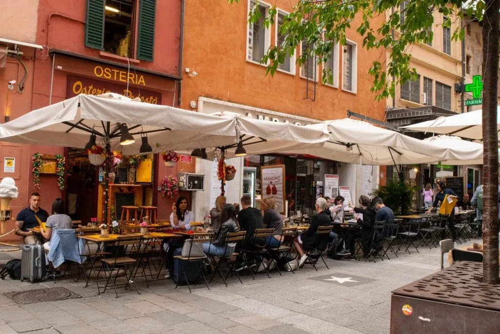 people eating outside at one of the restaurants bologna italy under white table umbrellas