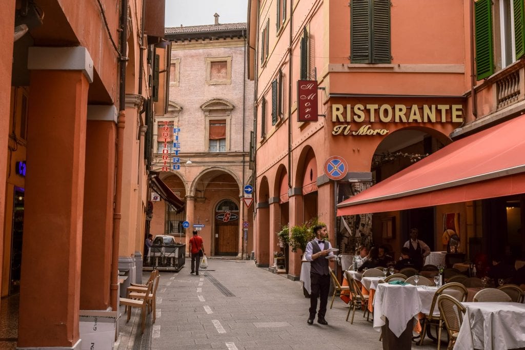 red buildings with porticoes on the side of the street in bologna italy