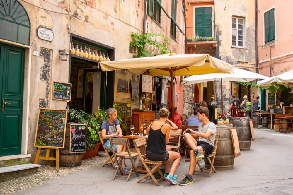 Photo of people sitting at a restaurant outside in Cinque Terre. There are umbrellas over the tables.