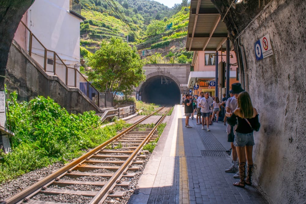 Hình ảnh đường ray xe lửa trống rỗng tại một nhà ga ở Cinque Terre.  Một số người đang đứng ở một bên và chờ đợi trên sân ga.