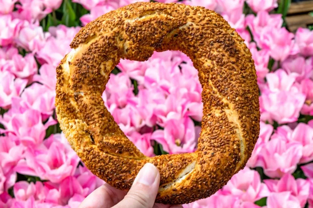 simit being held in front of pink flowers in istanbul turkey