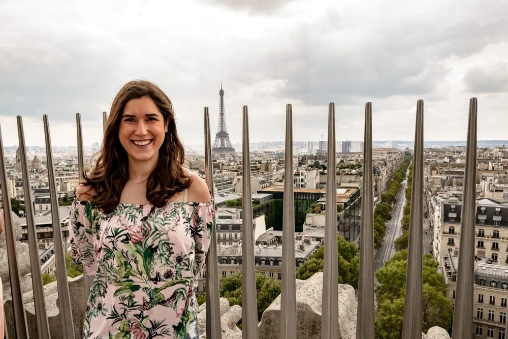 kate storm visiting arc de triomphe paris with metal spikes and eiffel tower in the background