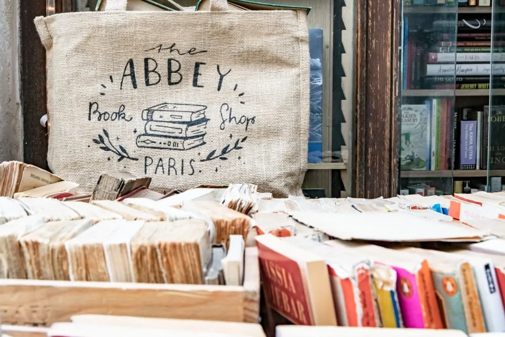 Photo from Abbey Bookshop in Paris. There are the tops of spines of books visible in the foreground and a tote bag that says "Abbey Bookshop" in the background.