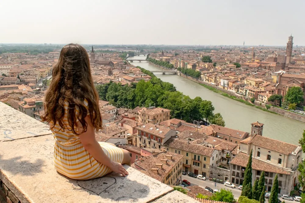 kate storm in a yellow dress sitting on a wall overlooking verona italy during a life of travel lifestyle