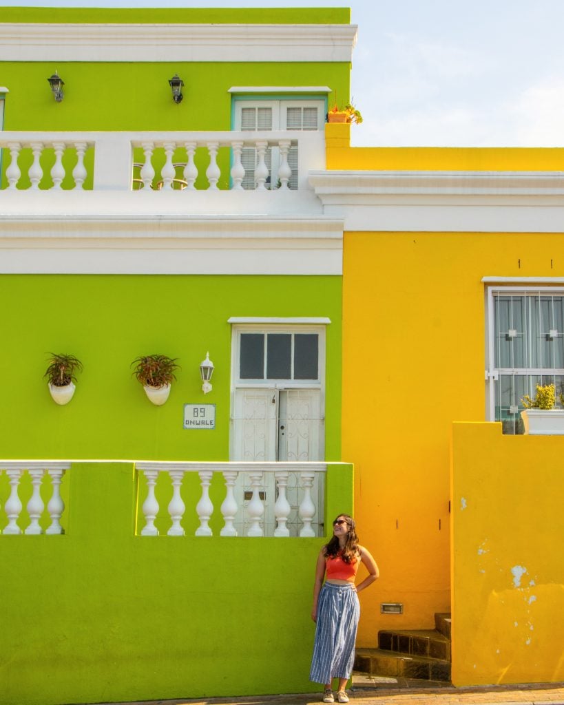 kate storm posing between a yellow and green building in bo kaap cape town