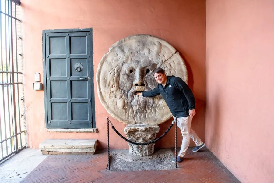 Jeremy standing with Mouth of Truth in Rome, wearing his favorite black jacket that always ends up on our packing list for Europe fall.