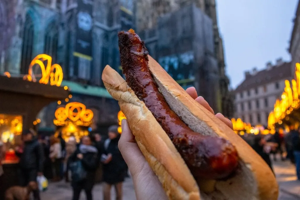 sausage roll being held up in front to the vienna cathedral during a trip to europe at christmas