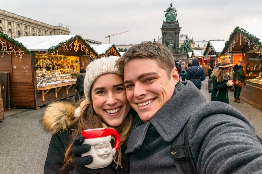 Kate and Jeremy in a Vienna Christmas market taking a selfie. Kate is holding up and red and white Santa mug.