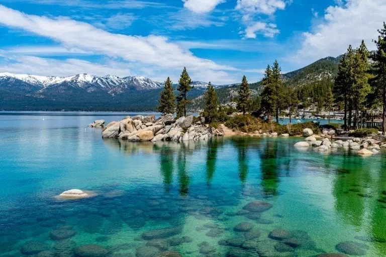 Clear water of Lake Tahoe California in summer with snowcapped mountains in the background--one of the best places to visit in the USA bucket list