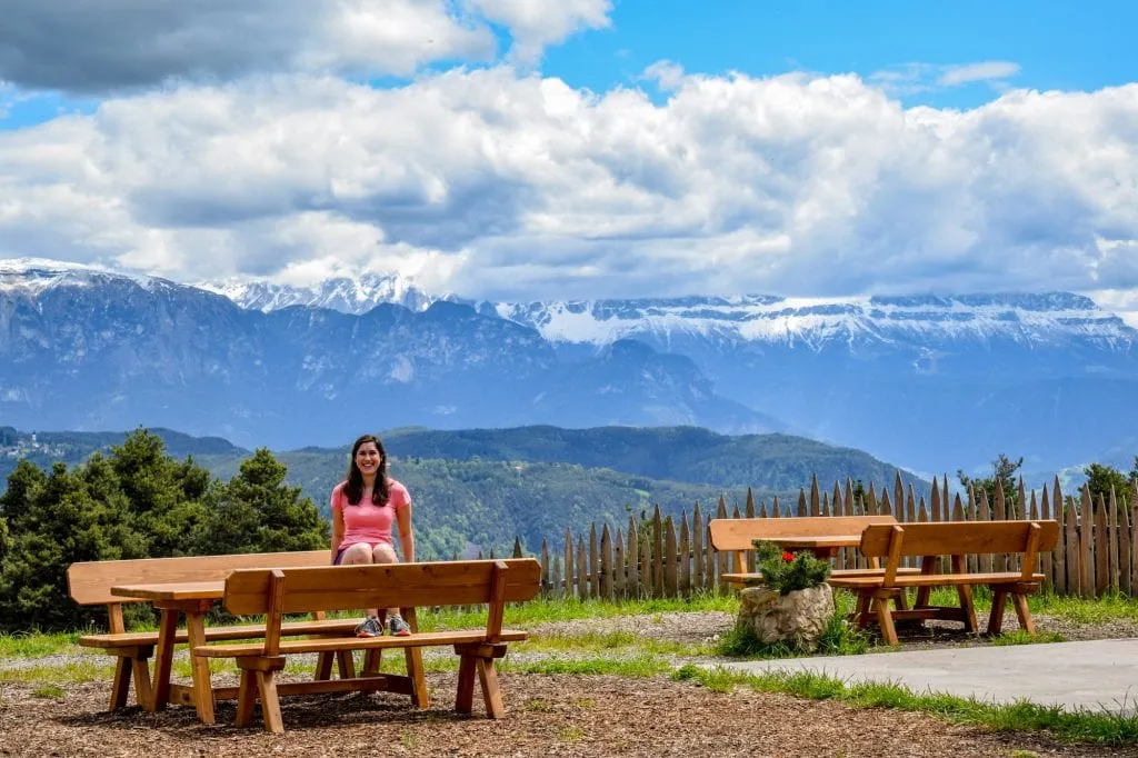 car trip around italy Kate Storm in a pink shirt sitting on a picnic table hiking in the Dolomites while on an Italy road trip
