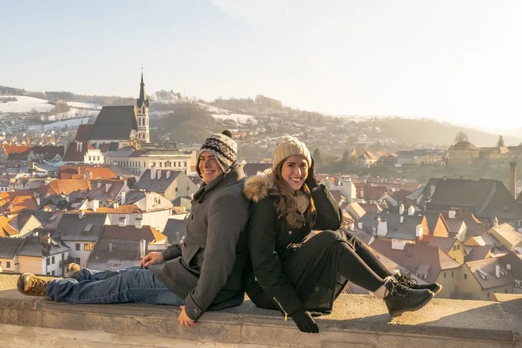 kate storm and jeremy storm sitting on a ledge overlooking cesky krumlov in winter