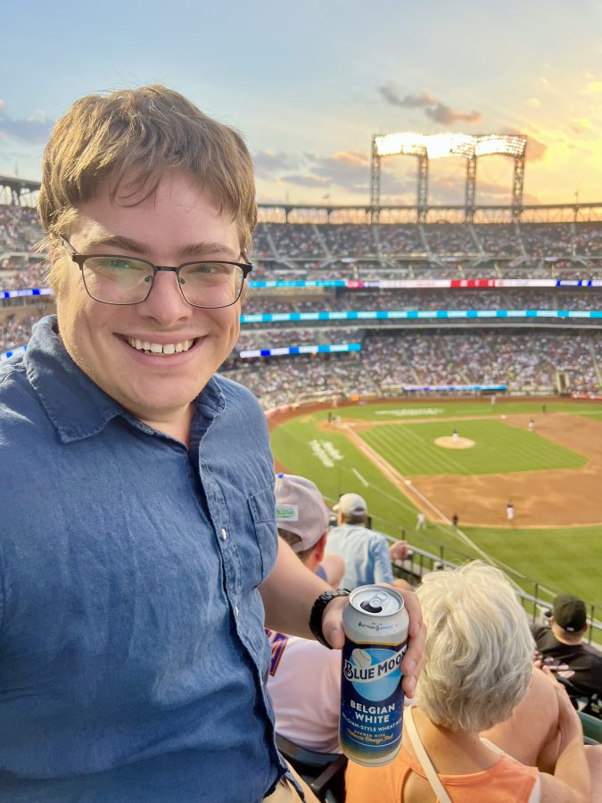 jeremy storm holiding a beer with the mets stadium and sunset behind him