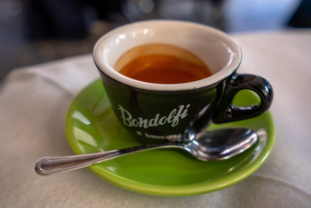 Shot of espresso close up in Rome on a green plate with a spoon resting on it--if you listen to any of these travel tips for Rome, be sure to remember to drink lots of espresso!