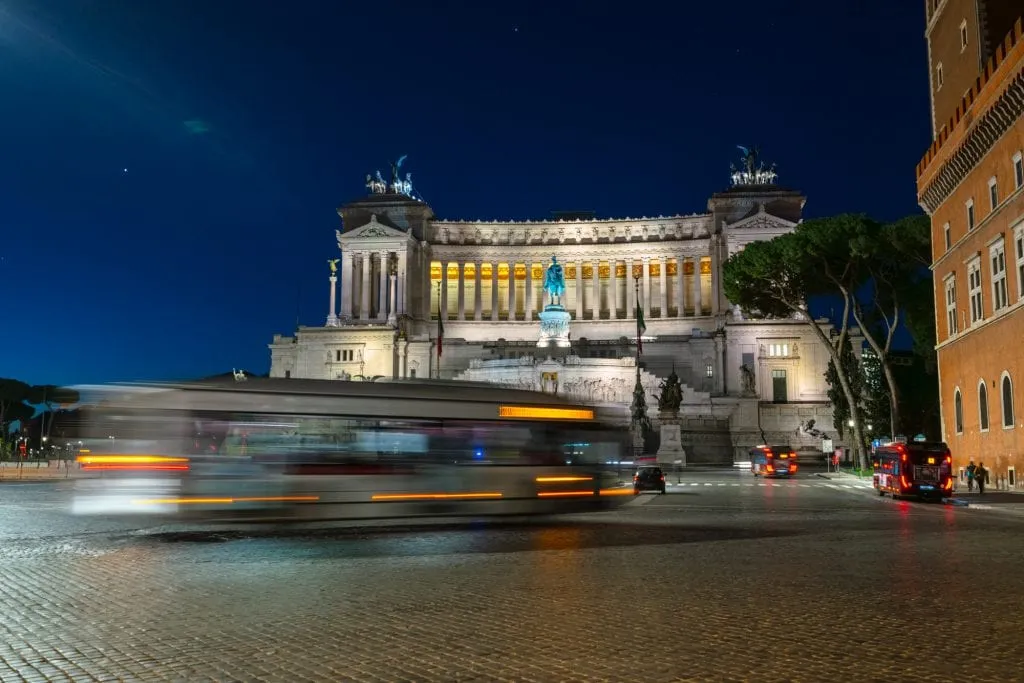 Altar of the Fatherland in Rome at night with a blurred bus passing in front of it