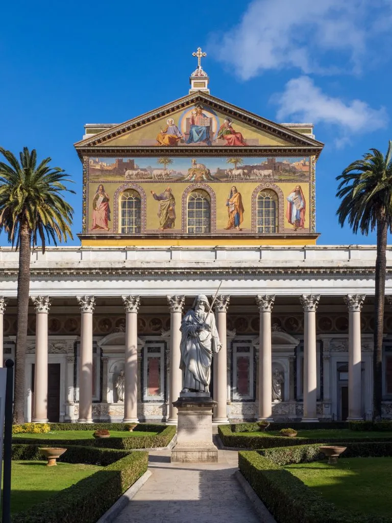 front facade of the basilica of st paul outside the walls framed by palm trees, one of the best hidden gems in rome italy