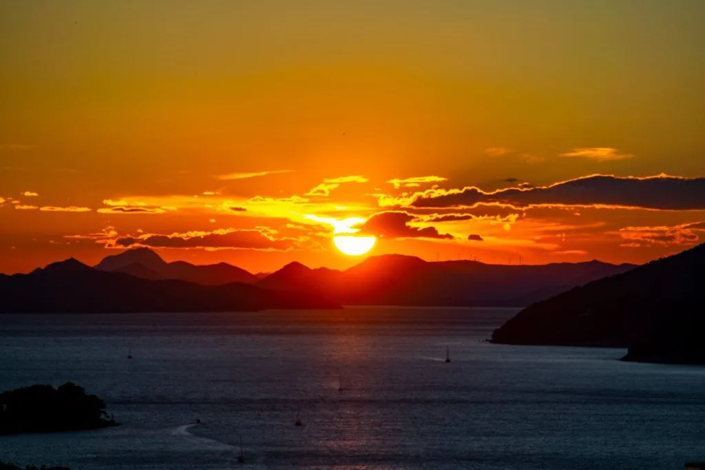 sunset over the water in dubrovnik with sailboats in the foreground