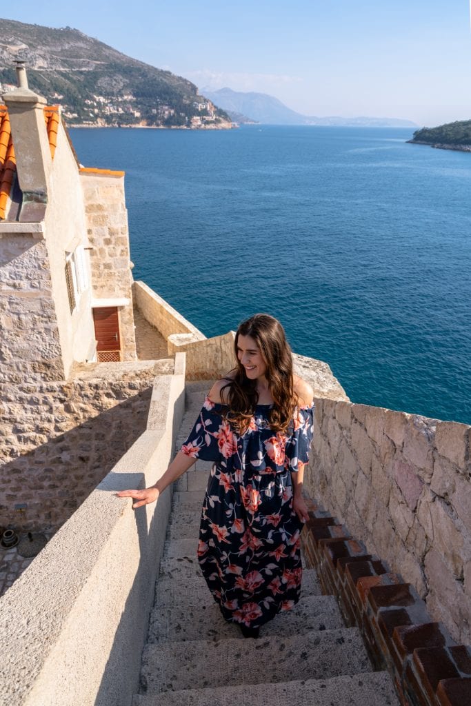 kate storm in a floral dress climbing a staircase along the dubrvonik city walls, one of the best things to do in dubrovnik croatia