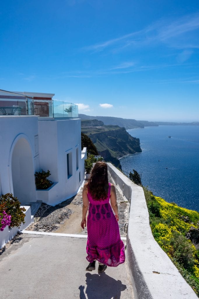 kate storm in a pink dress walking through a village in santorini greece