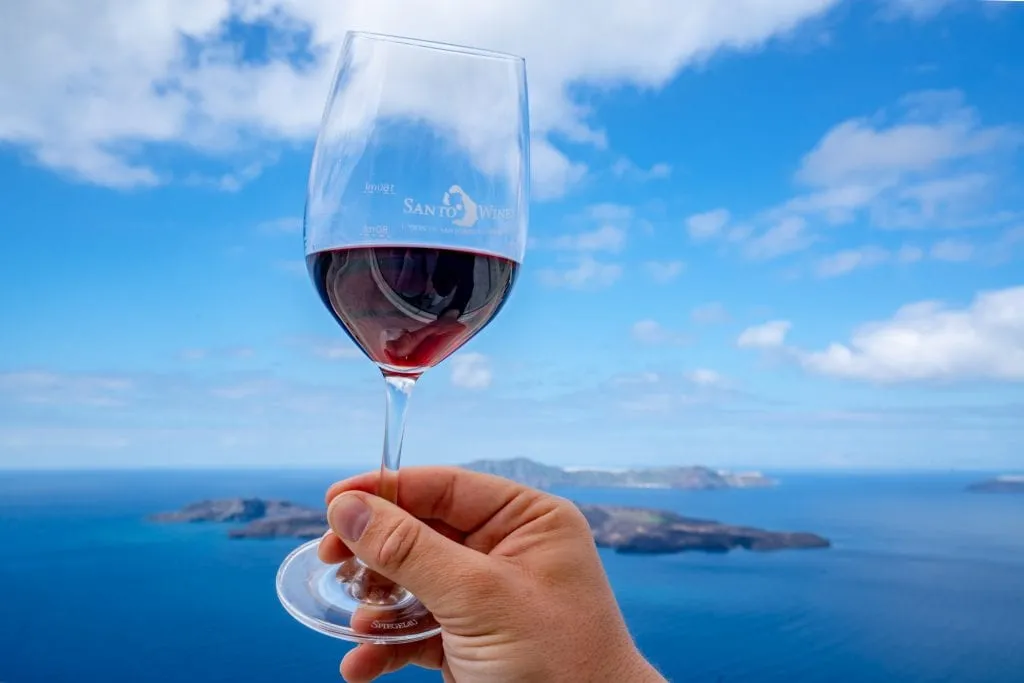 Glass of red wine being held up against sky, Honeymoon in Santorini