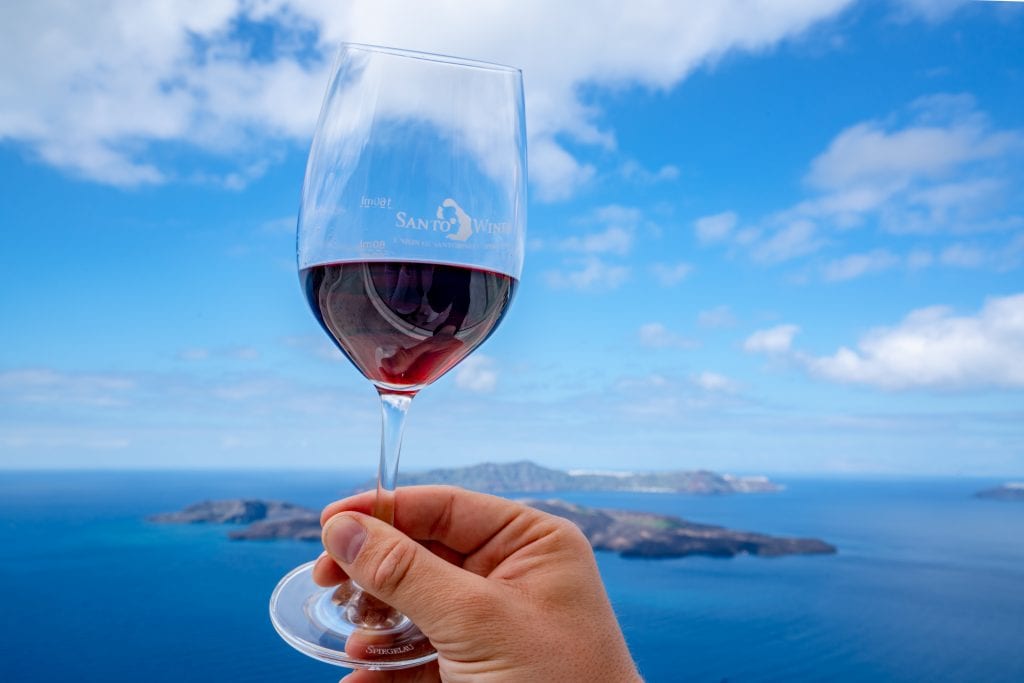 Glass of red wine being held up against sea, 3 day Santorini itinerary