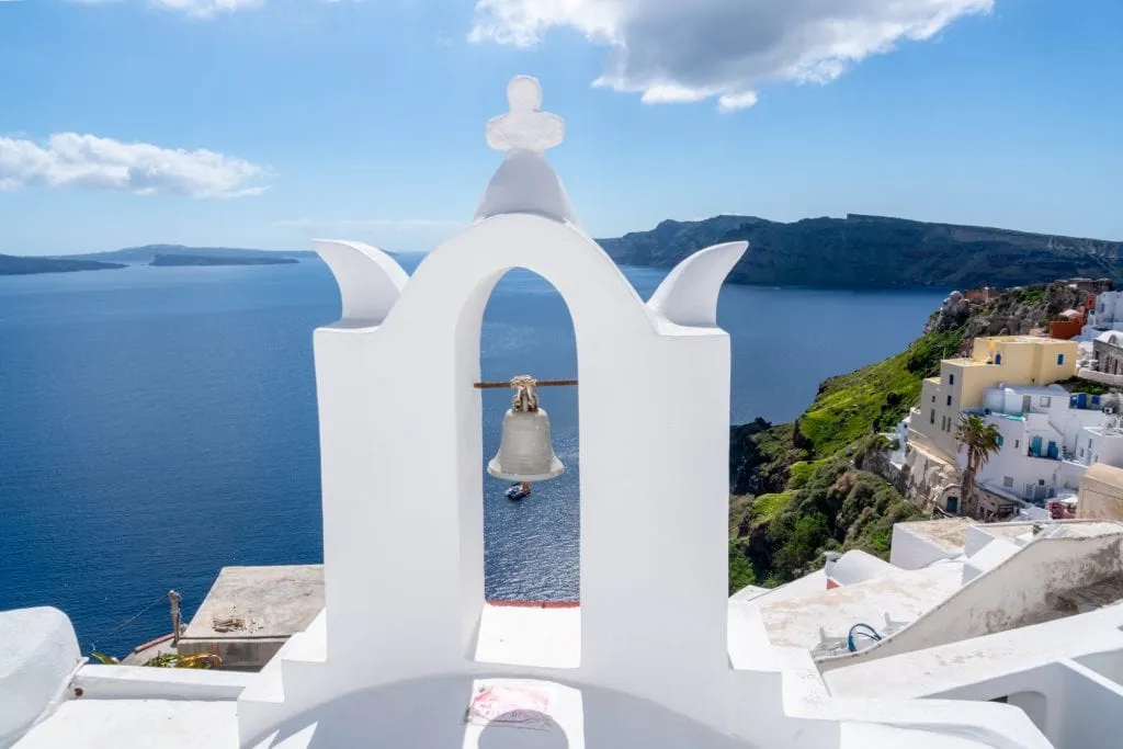 View of white bell tower in Santorini greece with caldera in the background