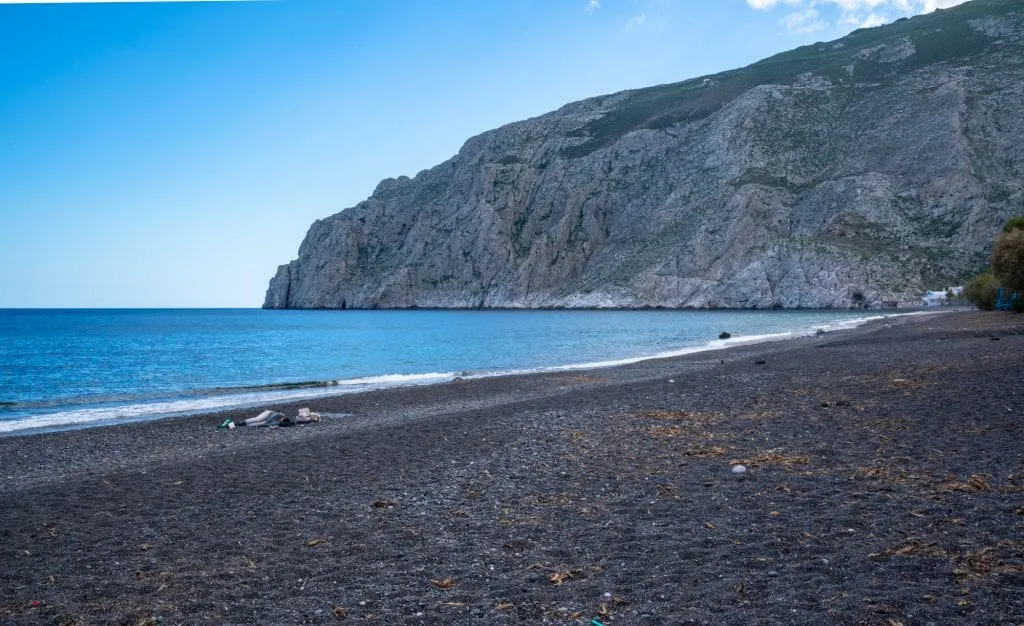 black sand beach of kamari greece with cliffs in the background