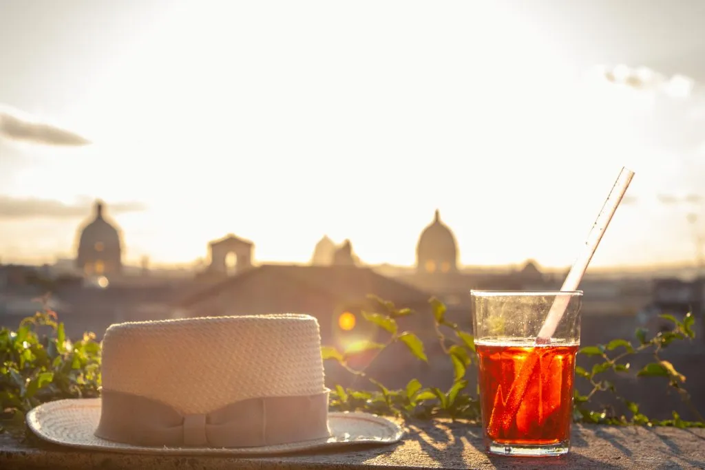 spritz and straw hat on the ledge of a rooftop during sunset in rome italy