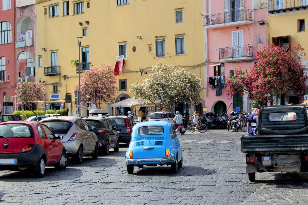 blue fiat driving through an area with several other cars in rome italy