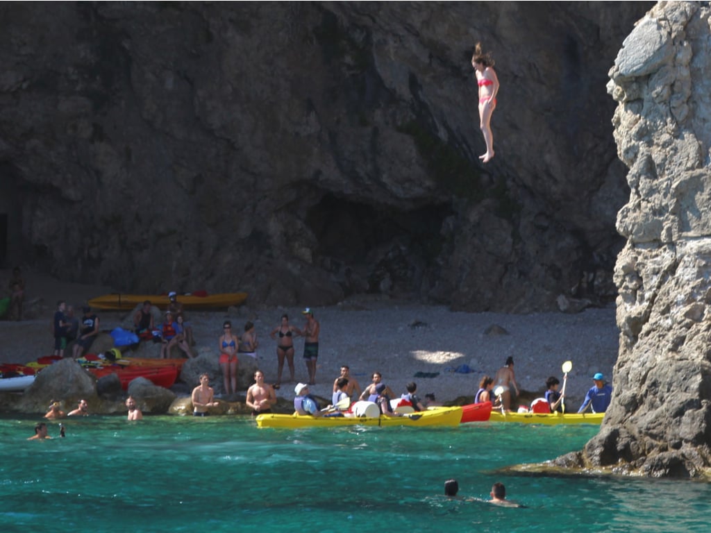girl cliff jumping in dubrovnik croatia with other swimmers and kayaks nearby