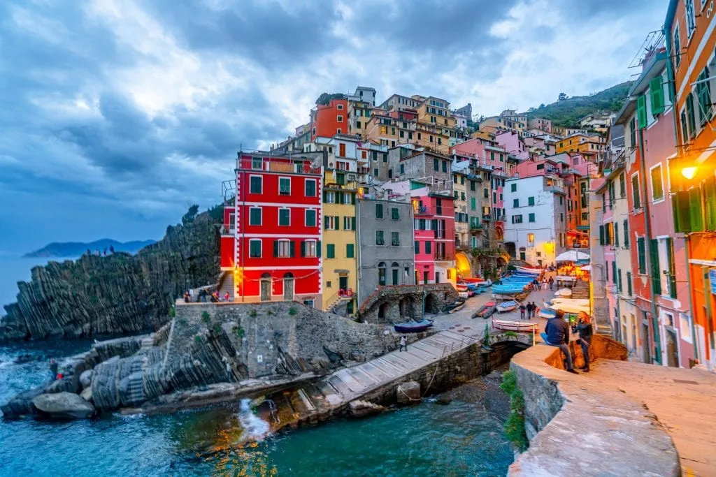 Riomaggiore at night, with lights showing lit up on colorful houses and the sea dark below.