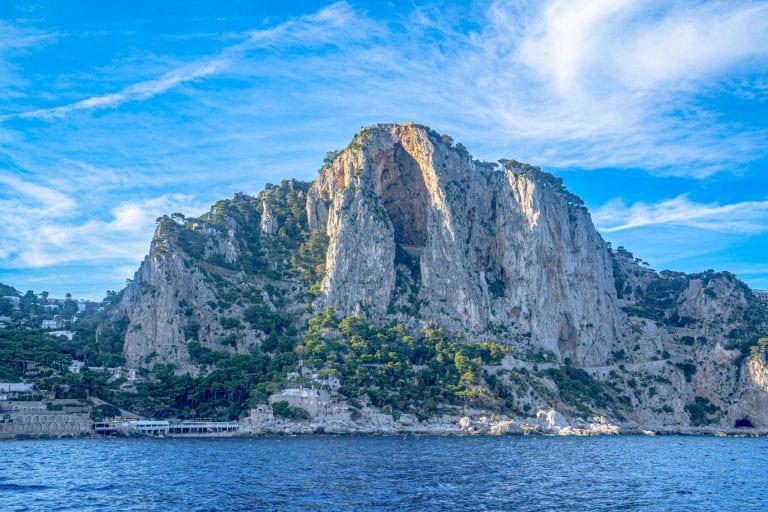 Photo of the island of Capri being approached by boat. You can see the sea at the bottom of the photo. Capri is an iconic destination to keep in mind when putting together your packing list for Europe summer!