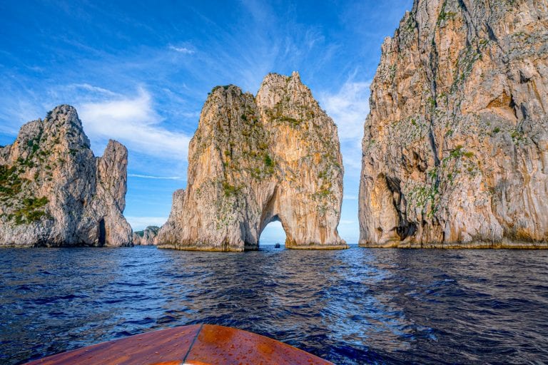 Faraglioni of Capri as seen from the water with the brown bow of a boat in the foreground. Capri is one of the most romantic places in Italy, partially because of the legend of the Faraglioni!