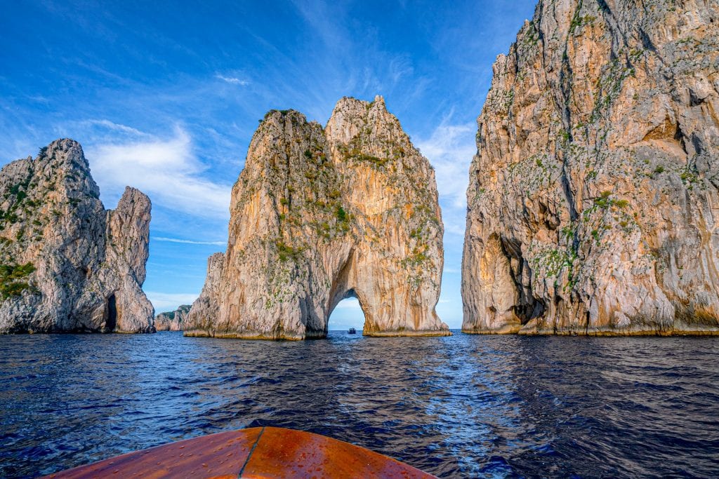 Close up photo of Faraglioni in Capri, the bow of a boat is visible in the bottom center of the photo