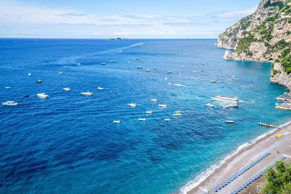 Water surrounding Amalfi Coast with boats on the water. There's a small piece of Positano's Beach visible in the bottom righthand corner of the photo.