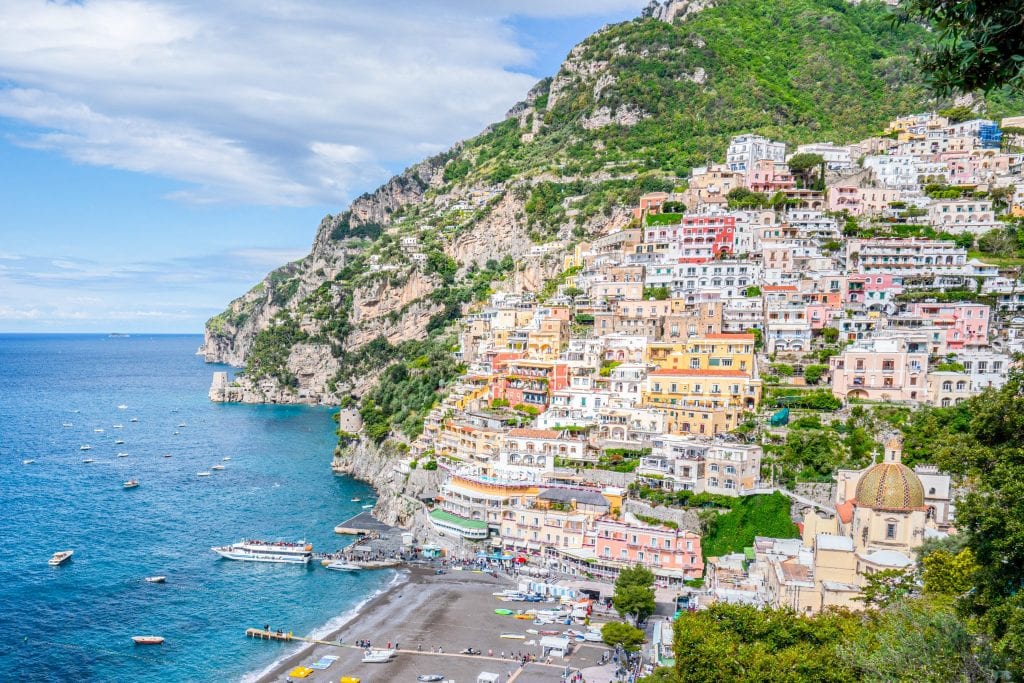 Photo of Positano from above. The town and cliff is on the right, beach at center bottom, and sea with boats to the left. Recommended stop on a 3 day Amalfi Coast itinerary.